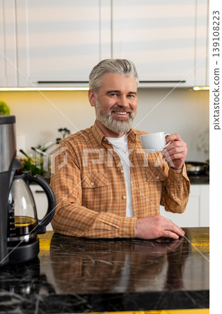 Middle-aged man pours fresh coffee from machine in kitchen enjoying morning routine energy at home 139108223