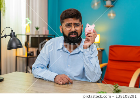 Indian man shakes empty piggy bank showing despair over bankruptcy debt seeking cash money loss sad Indian man shakes empty piggy bank showing despair over bankruptcy debt seeking cash money loss sad 139108291