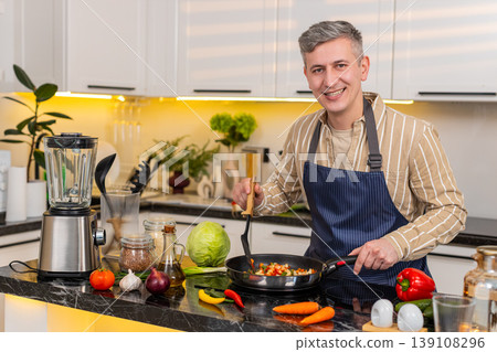 Middle-aged man smiling while stirring vegetables in frying pan in kitchen at home for healthy meal Middle-aged man smiling while stirring vegetables in frying pan in kitchen at home for healthy meal 139108296