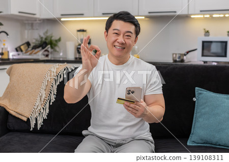 Asian man completes payment with smartphone and credit card smiles at confirmation shows thumbs up Asian man completes payment with smartphone and credit card smiles at confirmation shows thumbs up 139108311