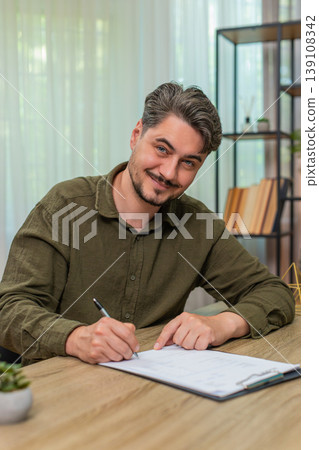 Middle-aged man satisfied signs documents approving content signing paperwork gladly at table desk 139108342