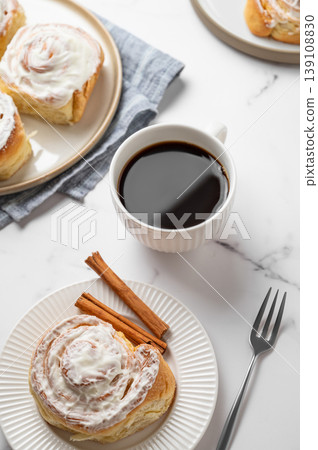 Freshly baked cinnamon rolls with white icing and a cup of black coffee on a light marble background Freshly baked cinnamon rolls with white icing and a cup of black coffee on a light marble background 139108830