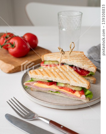 Club sandwich with ham, cheese, tomatoes, lettuce, cucumber on a plate on a white table 139108833