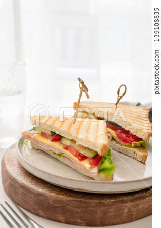 Club sandwich with ham, cheese, tomatoes, lettuce, cucumber on a plate on a wooden board Club sandwich with ham, cheese, tomatoes, lettuce, cucumber on a plate on a wooden board 139108835