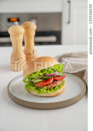 Beef burger with tomato, cheese, and lettuce on a plate on a light table with spice 139108839