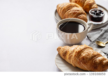 Cup of espresso coffee and fresh croissants on a light background with berry jam and spoon close up. 139108850