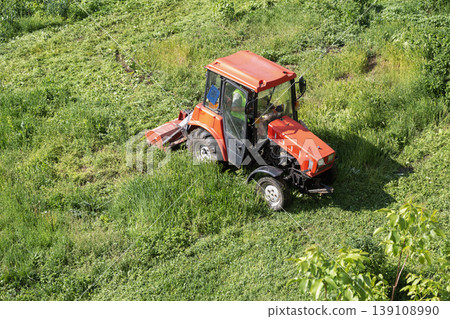 A small red tractor with a lawnmower cutting grass on a lawn. 139108990