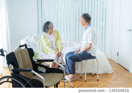 A senior couple sitting on a bed and a wheelchair 139109018
