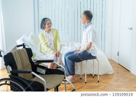 A senior couple sitting on a bed and a wheelchair 139109019