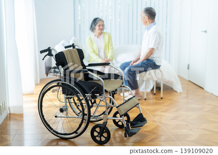 A senior couple sitting on a bed and a wheelchair 139109020