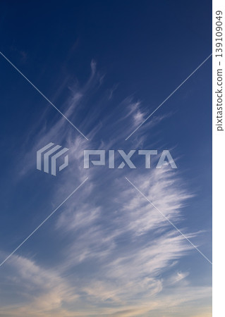 White cirrus uncinus clouds drifting in blue sky with golden sunset glow. White cirrus uncinus clouds drifting in blue sky with golden sunset glow. 139109049