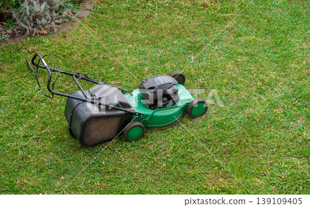 Gasoline lawn mower on freshly cut grass in backyard,garden maintenance equipment for trimming lawn and keeping yard neat and well maintained outdoors Gasoline lawn mower on freshly cut grass in backyard,garden maintenance equipment for trimming lawn and keeping yard neat and well maintained outdoors 139109405