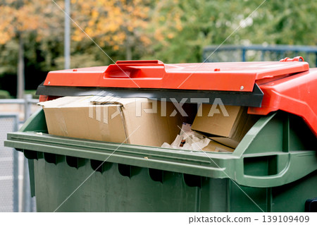 Green trash container filled with cardboard boxes and paper waste, recycling and waste management concept in urban environment on sunny day 139109409
