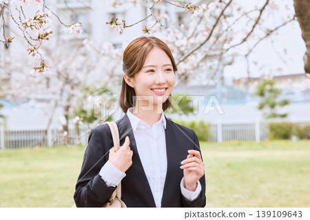 A young woman in a business suit smiles under cherry blossoms – an image of spring job hunting. A young woman in a business suit smiles under cherry blossoms – an image of spring job hunting. 139109643