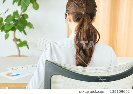 一位女商務人士在辦公室的辦公桌前工作，鏡頭從背後拍攝；一位身穿西裝、綁著馬尾辮的公司員工。 139109662