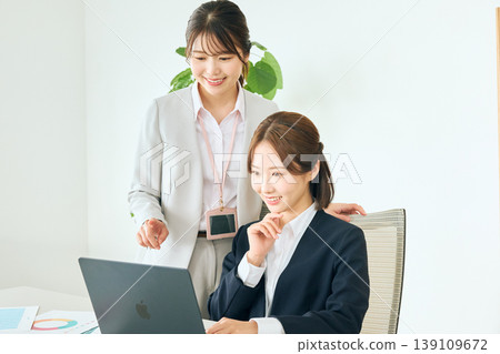 兩位年輕的女性商務人士,一位資深,一位初級,正在辦公室開會,她們看著各自的筆記型電腦螢幕。 兩位年輕的女性商務人士,一位資深,一位初級,正在辦公室開會,她們看著各自的筆記型電腦螢幕。 139109672