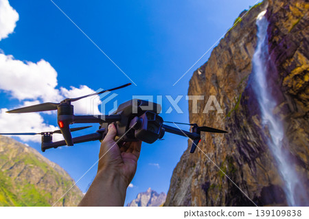 Hand holding drone near dramatic waterfall and mountains Hand holding drone near dramatic waterfall and mountains 139109838