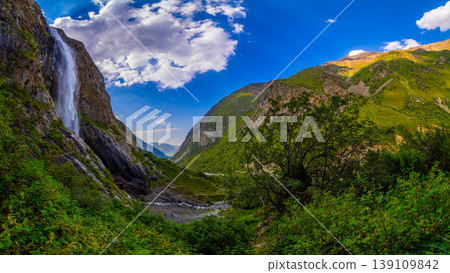 Majestic waterfall cascading down rocky cliff in lush valley 139109842