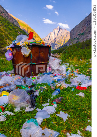 Overflowing trash bin surrounded by plastic waste in valley 139109852
