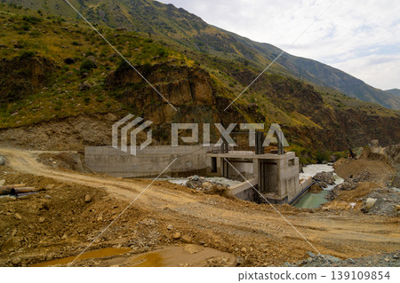 Concrete hydroelectric dam structure under construction in mountainous landscape 139109854