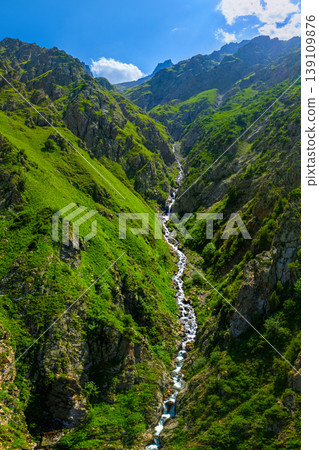 Majestic mountain valley with cascading stream and green slopes 139109876