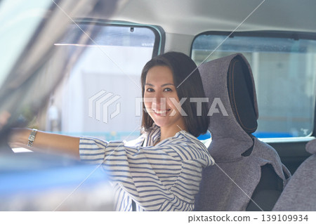 A Japanese woman is sitting in the driver's seat of a car, holding the steering wheel and smiling at the camera. A Japanese woman is sitting in the driver's seat of a car, holding the steering wheel and smiling at the camera. 139109934