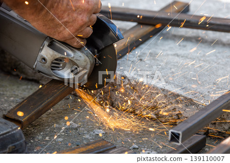 Close-up of angle grinder cutting metal tubes on concrete ground 139110007