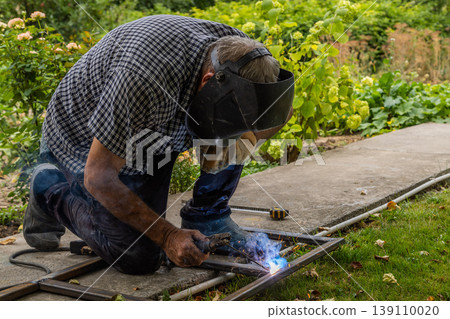 Person welding metal frame outdoors with sparks flying Person welding metal frame outdoors with sparks flying 139110020