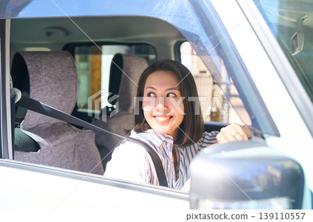 A Japanese woman smiles as she holds the steering wheel in the driver's seat of a car. A Japanese woman smiles as she holds the steering wheel in the driver's seat of a car. 139110557
