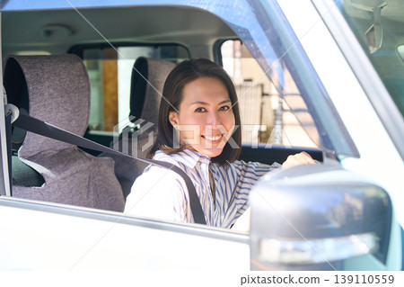 A Japanese woman is sitting in the driver's seat of a car, holding the steering wheel and smiling at the camera. A Japanese woman is sitting in the driver's seat of a car, holding the steering wheel and smiling at the camera. 139110559