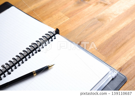 圖片顯示的是一個人在書桌前工作，桌上打開一本活頁筆記本。 139110687