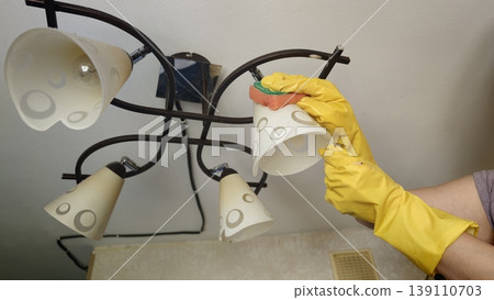 Cleaning light fixtures in a kitchen during daytime tasks to maintain cleanliness Cleaning light fixtures in a kitchen during daytime tasks to maintain cleanliness 139110703