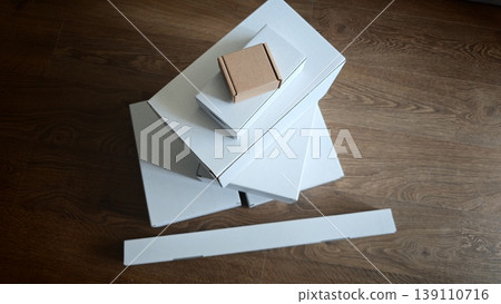 Stack of white boxes with a small brown box on top on wooden floor Stack of white boxes with a small brown box on top on wooden floor 139110716