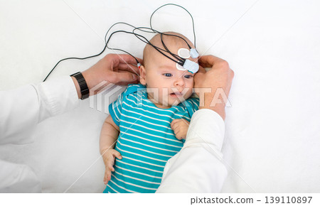 Newborn hearing screening and diagnosis at the hospital. Baby having hearing screening with special electrodes on his head and ear Newborn hearing screening and diagnosis at the hospital. Baby having hearing screening with special electrodes on his head and ear 139110897