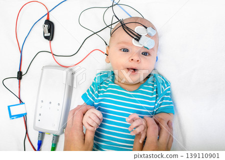 Newborn hearing screening and diagnosis at the hospital. Baby having hearing screening with special electrodes on his head and ear 139110901