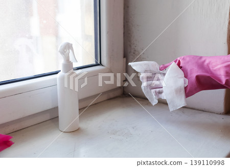 Person in pink gloves cleaning mold on window sill and walls using antifungal spray. Removing toxic black mold and mildew from window frame and plaster. Home maintenance and hygiene. 139110998