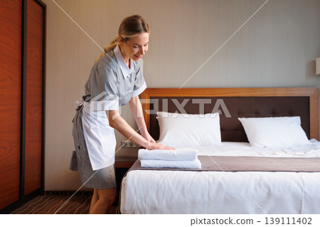 Housekeeper carefully arranging folded towels on hotel bed in guest room Housekeeper carefully arranging folded towels on hotel bed in guest room 139111402