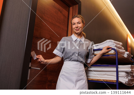 Housekeeping worker using key card at hotel room door with fresh linens on service cart 139111644