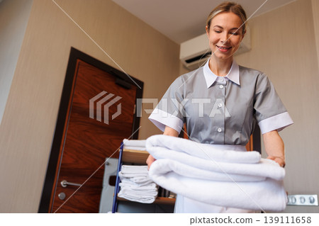 Professional maid arranging folded towels on bed during hotel room cleaning Professional maid arranging folded towels on bed during hotel room cleaning 139111658