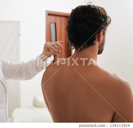 Reflexologist's hand with acupuncture needle while insert needle into special point on man's body meridians for treatment. Back view Reflexologist's hand with acupuncture needle while insert needle into special point on man's body meridians for treatment. Back view 139111924