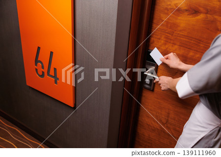 Hotel housekeeper opening guest room door with keycard in modern hallway closeup Hotel housekeeper opening guest room door with keycard in modern hallway closeup 139111960