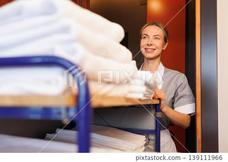 Smiling female housekeeper behind linen trolley delivering fresh towels to room Smiling female housekeeper behind linen trolley delivering fresh towels to room 139111966