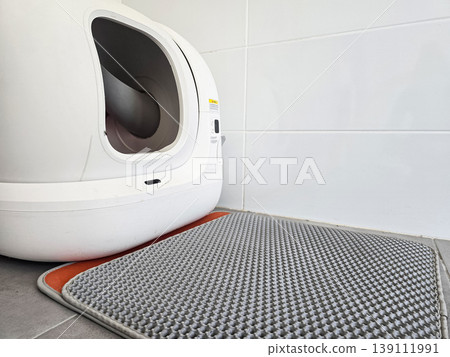 Modern automatic self-cleaning cat litter box placed on a tiled floor with a mat. Concepts of pet care technology, home convenience, and smart living solutions. 139111991