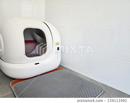 Modern automatic self-cleaning cat litter box placed on a tiled floor with a mat. Concepts of pet care technology, home convenience, and smart living solutions. 139111992