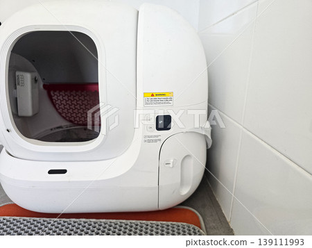 Modern automatic self-cleaning cat litter box placed on a tiled floor with a mat. Concepts of pet care technology, home convenience, and smart living solutions. 139111993