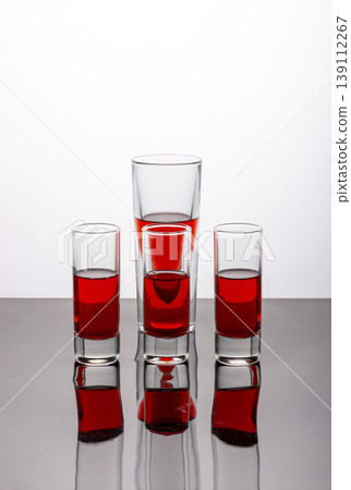 Four glasses of red drink on a reflective surface Four glasses of red drink on a reflective surface 139112267