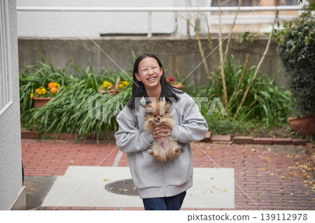A middle school girl playing with a cute Pomeranian puppy in the garden of her apartment building in springtime. 139112978