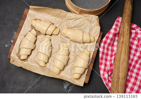 Uncooked croissant blanks on parchment paper and kitchen utensils on a dark background Uncooked croissant blanks on parchment paper and kitchen utensils on a dark background 139113165