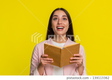 Young woman reading book with wide open eyes amazed expression intrigued thrilling surprising plot 139113362
