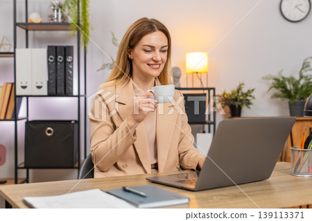 Businesswoman focuses on laptop coffee cup hand takes sip enjoys taste gains energy boost for work 139113371